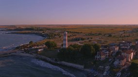 Aeriel footage of an old lighthouse, the waves crashing on the shore while the sun is setting. The oldest lighthouse in Bulgaria.