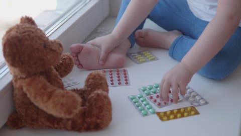 Toddler sits on windowsill and plays with scattering pills without parent's control. Dangerous situation with little boy. Medicines are freely available to child.