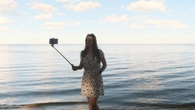 Happy woman having video call with smartphone and monopod in the background of the sea horizon at sunset