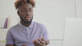 A black man with dreadlocks communicates virtually via the Internet, online training: a teacher, a mentor conducts a lesson using a laptop. A man at a table in a bright room with daylight