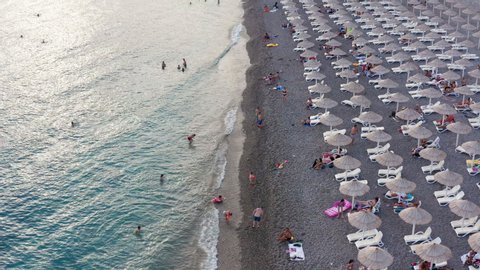Rows of reed umbrellas at the sandy beach in Canj, on the Adriatic coast of Montenegro. People on vacation under sunshades, or in blue and turquoise sea. Impact of coronavirus pandemic on tourism.