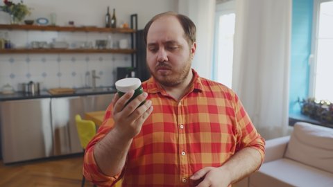 Portrait of overweight man reading instructions on bottle with slimming pills standing at home. Unhealthy way to get slim, weight loss, dieting, fat burning, pharmacy, medicine concept