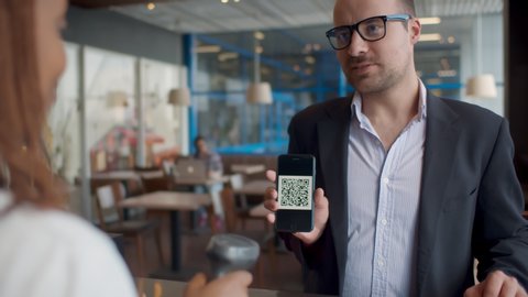 Businessman pay by scanning QR code on smartphone in coffee shop. Man customer using qr-code on smartphone for payment to owner at cafe. Small business and cashless technology concept