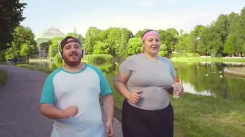 Overweight young couple running together in summer park. Fat man and woman working out together and jogging outdoors, Healthy lifestyle and sport concept