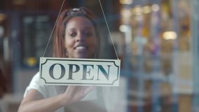 Small business African-American female owner smiling while turning sign for opening of cafe. Happy waitress in apron turning sign on door opening restaurant in the morning - Powered by Shutterstock - Get 15% off with code: PIKWIZARD15