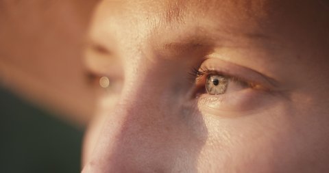 Close up portrait of a young gardener or farmer woman eyes looking at beautiful evening sunset sunlight or golden light wearing a hat macro slow motion