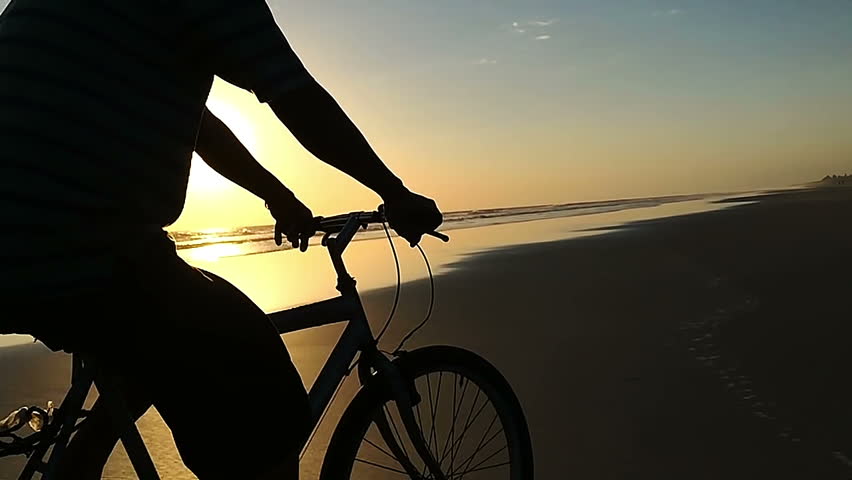 A silohuette of a man riding a bike on the afternoon at the beach