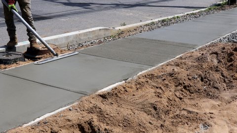 Construction mason building a screed coat cement a laborer floats a new concrete sidewalk