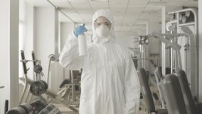 Middle shot of serious woman in protective suit and respirator spraying disinfectant in gym. Portrait of concentrated Caucasian employee posing in sports club with sanitizer. Covid-19 lifestyle. - Powered by Shutterstock - Get 15% off with code: PIKWIZARD15