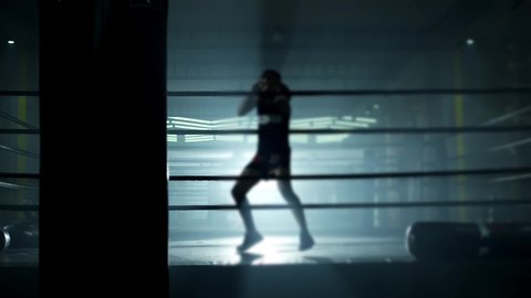 Kickboxer training in low light gym . Muay thai fighter punching . Silhouette on dark background. Boxer training in ring. Silhouette . Cinematic slow motion shot of a professional young man practicing