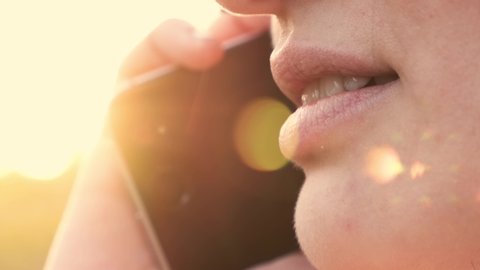 Young Woman Talking on Mobile Phone. Close Up Shot of Speaking Mouth on Outdoor. Lens Flare on Background on Sunset. B Roll.  4K Resolution UHD.