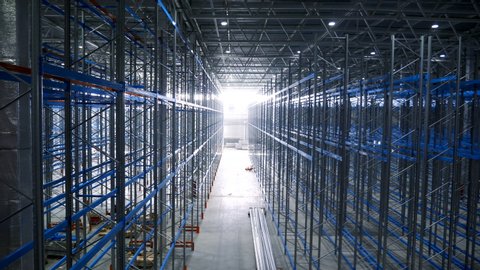 Point of View Empty Warehouse With Metal Shelves. Large Modern Industrial Building From The Inside With Rows Racks. Big Steel Structures of Pallet Frame in Sorting Center of the Logistics Company 4k