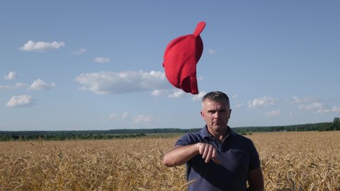 Belarus, Minsk, June 2020. Mature farmer, former trump supporter standing in the wheat fields, removing MAGA hat unsatisfied in Trump's policies and throwing at the camera