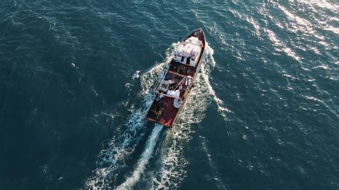 Fishing boat flying drone with large catch fish swirling hungry gulls flock of glaruses aerial view slow motion. Small ship floats on sea surface leaving a path of sea foam water. Top view. Copy space