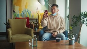 Asian Man in quarantine for coronavirus wearing protective mask with filter, he's working from home and using smartphone. Video call. Video conference with mobile phone.