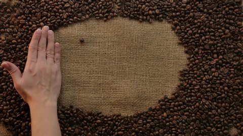 Lettering italian word caffe made of coffee beans on burlap. Elegant hand waving and inscription appears. Traditional jute bag with arabica grains surface horizontal top view. Slow motion