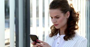 Close up of confident business lady in white suit standing on city center and holding smartphone. Young brunette looking at camera and using gadget outdoors.
