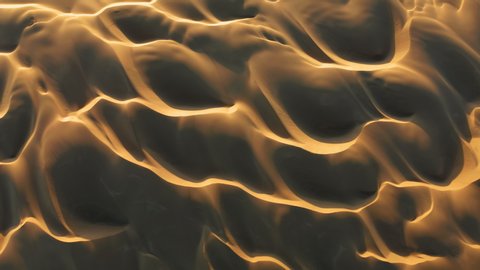 4K drone horizontal view on the abstract pattern in the shape of ocean waves. Beautiful aerial landscape. Wild desert nature at sunset. Top down view on golden sand hills highlighted by the last sun.