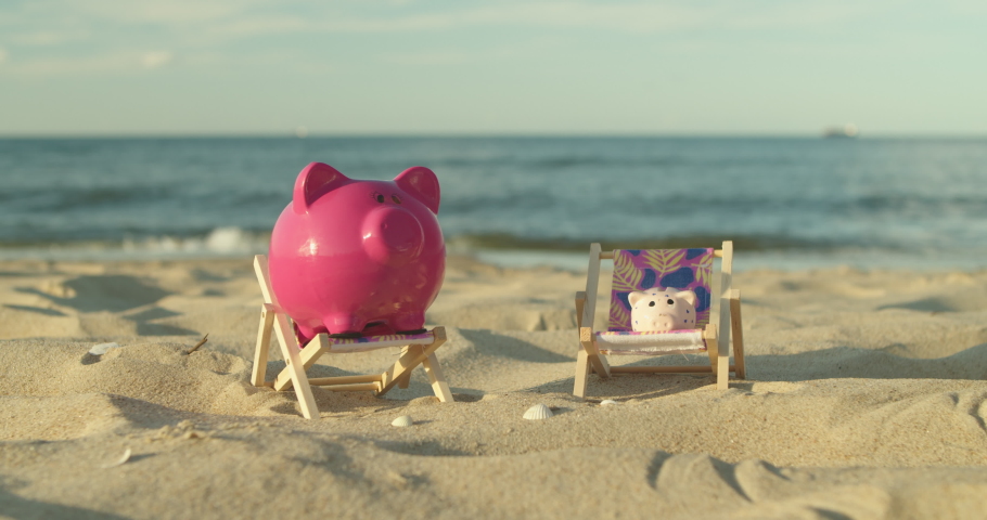 
Two piggy banks sit on mini sun loungers on the sandy beach. A man's hand throws a coin into a piggy bank. Male Hand Throws a Coin Into a Piggy Bank a Pig on a Sandy Shore. Slow Motion. Royalty-Free Stock Footage #1056596033