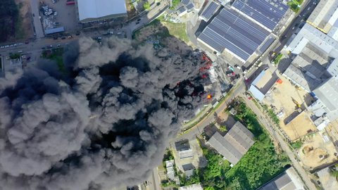 Aerial, top down above firefighters trying to quell the fire, in front of a building on fire, a huge black smoke cloud, in Haina, San Cristobal, Dominican Republic - screwdriver, drone shot