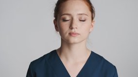 Young attractive female doctor calm down on camera over gray background. Tired expression