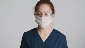 Female doctor in protective eyeglasses, mask and medical gloves coughing over white background. Feeling bad expression