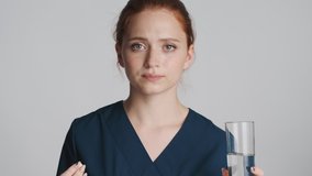 Portrait of attractive female doctor taking medical pills and drinking pure water over white background