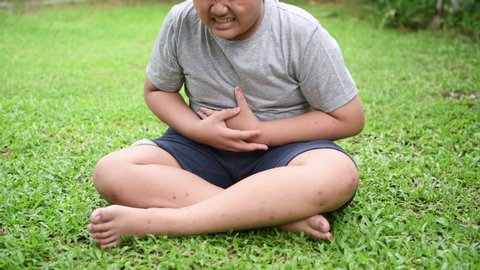 Obese fat boy sitting and suffer from stomachache on the lawn Because food poisoning
