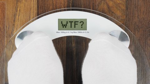 Overweight on bathroom scales digital display with an inscription WTF. Concept of tackling overweight and obesity. A woman steps on the scales to check her weight. Close-up view
