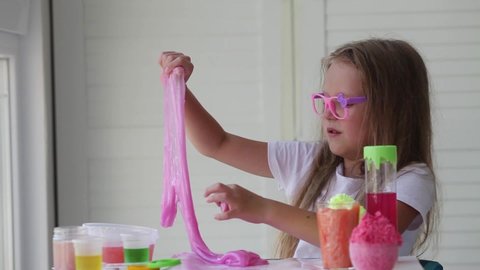 Little girl stretching pink slime to the sides.Slime fell and the girl laughs. Kids hands playing slime toy. Making slime. Copyspace.