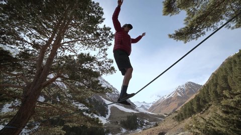 A young man teeters on a slackline in the mountains of the north Caucasus. Slackline en background of the mountains