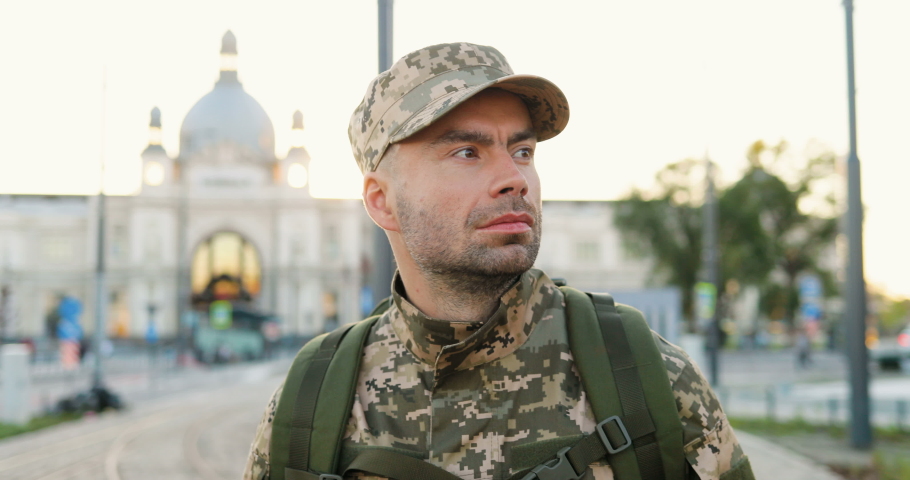 Caucasian young brave male soldier in uniform, hat and with backpack walking outdoor. Confident militarian officer strolling the street in military clothes. Going to army or coming back. Royalty-Free Stock Footage #1056609515