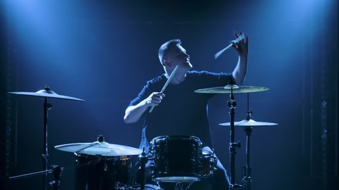Silhouette drummer playing on drum kit on stage in a dark studio with smoke and neon lighting. Performance vocal and musical band. Slow motion.