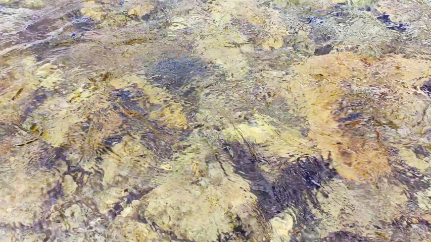 Close-up of the water surface and yellow and broun stones. Pure clean river water is running. 4k video