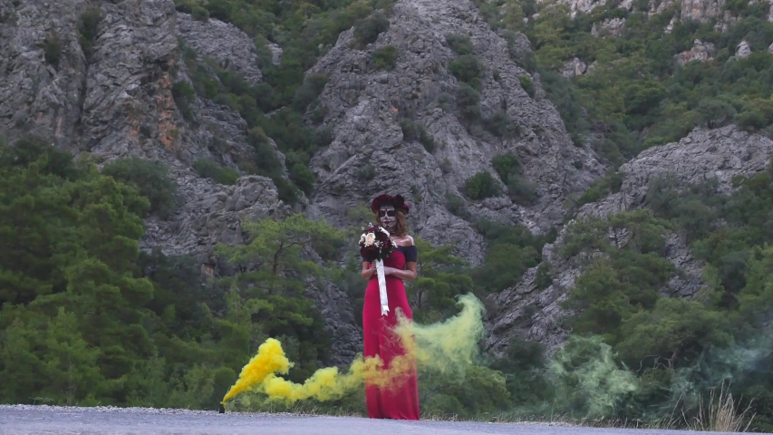 Santa Muerte girl in pink dress with bouquet on Halloween eve outdoors in yellow smoke