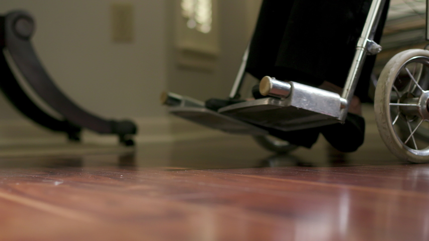 Wheels casting shadows on a shinny floor as a woman in a wheelchair pushes herself slowly along.