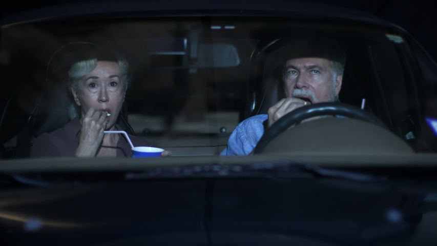 A mature Caucasian couple sitting in their car watching a funny movie at a drive-in theater. Royalty-Free Stock Footage #1056614870