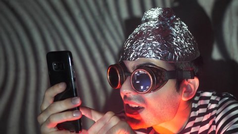 Insane men in a fantasy world wearing a thin foil cap and using his mobile phone. A crazy individual acting in a strange way due to conspiracy theories.
