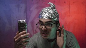Insane men in a bunker video calling with his smartphone. He is wearing a tinfoil hat because he is mentally sick and scared of what's happening in the world.