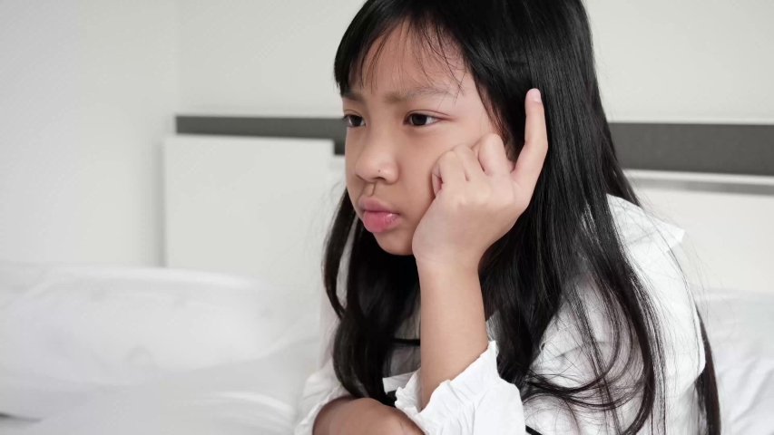 Asian child girl wearing a white shirt is contemplating or worried about something