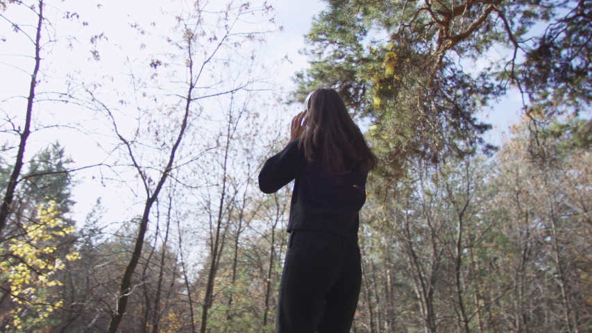 4K portrait of attractive woman in headphones listening to music and moving rhytmically smiling with delight in autumn forest. Low angle 360 degree tracking arc shot.