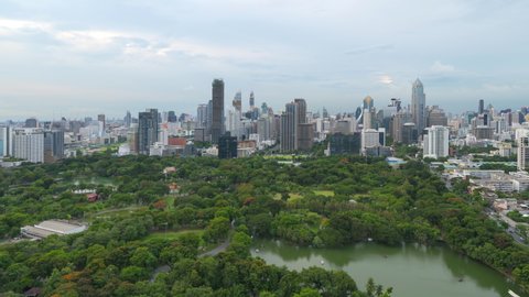 Time lapse of aerial view of green trees in Lumpini Park, Sathorn district, Bangkok Downtown Skyline. Thailand. Financial district and business center in smart urban city in Asia. Skyscraper buildings