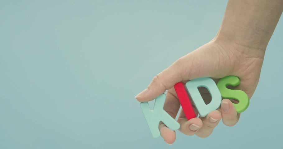 The hand pull out of the water the word "kids", which is spelled out of colorful plastic letters.