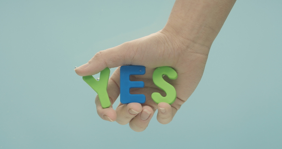 The hand is slowly moving under the water and holding the word "yes", which is made out of green and blue plastic letters.