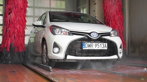 WROCLAW, POLAND - JULY 19, 2020: Equipment of automatic car wash. White Car Toyota Yaris hybrid being wash by big red brush.