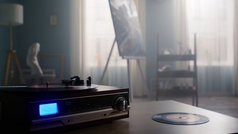 Retro vinyl player is on the table, with vinyl record on, vinyl record is beside the recorder, classical music is heard in cozy art studio, creating atmosphere of magic and inspiration, Slow motion.
