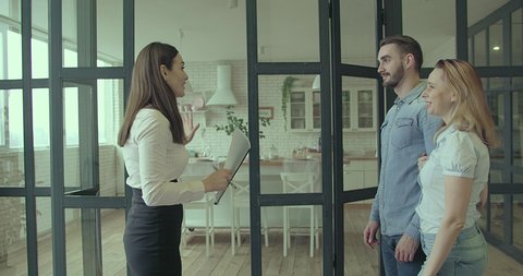 Happy Couple with real-estate agent visiting house for sale or for rent, Young man and woman cheerful at home. Loving people buying an apartment. Immovables market 4K slow motion video.