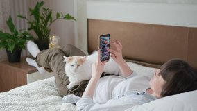 food delivery, young female shopper uses an app on smartphone and orders groceries from a store lying at home on bed with cat during isolation at lockdown due to pandemic and coronavirus, social - Powered by Shutterstock - Get 15% off with code: PIKWIZARD15