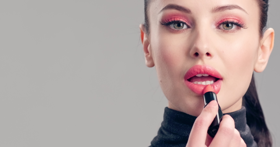Young woman paints her lips with lipstick. Beautiful brunette model doing make-up. Woman makes makeup before camera.  Cosmetic concept. 4k Slow motion footage. Closeup view. | Shutterstock HD Video #1056632822