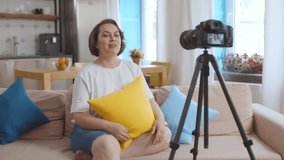 Female obese blogger recording video for overweight people sitting on couch at home. Plus size pretty lady filming video for internet blog about body positive and healthy lifestyle